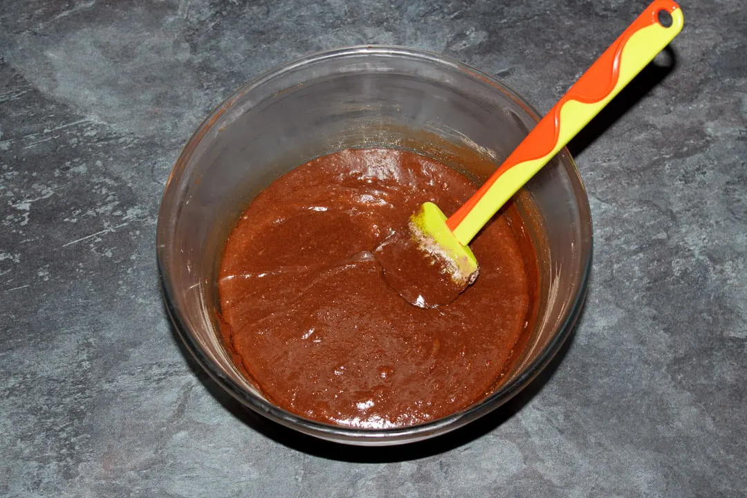 Chocolate brownie batter in a glass bowl with a green spatula