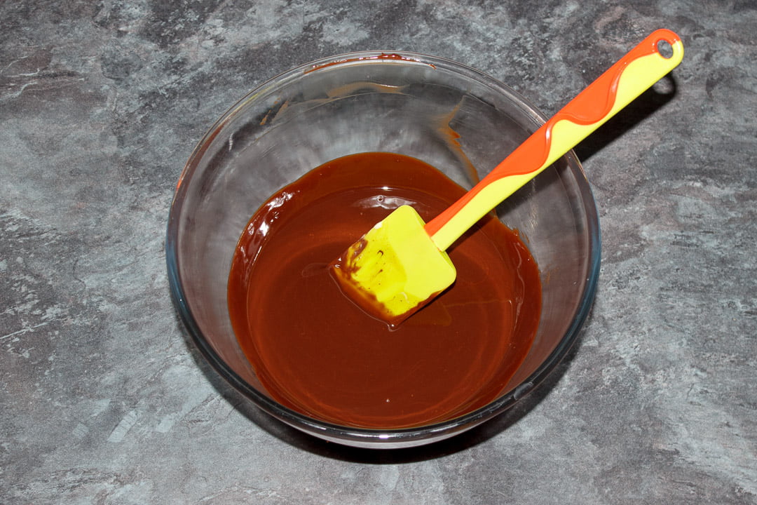 Butter and dark chocolate melted together in a glass bowl with a green spatula