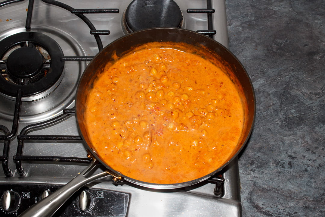 Chana masala simmering in a large frying pan on a stove