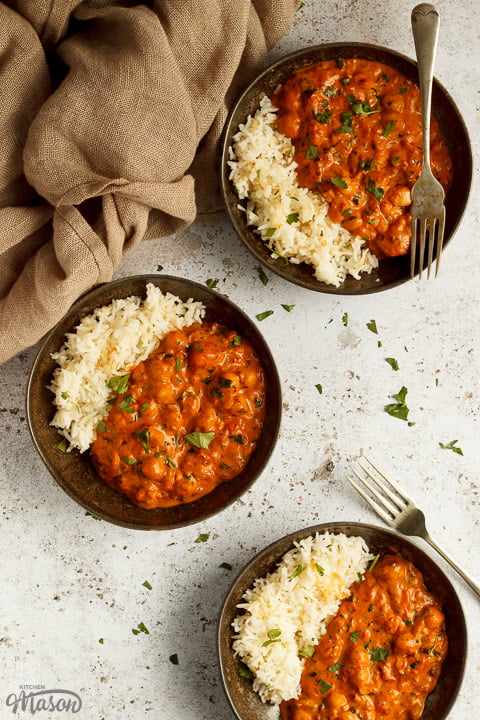 3 bowls of chana masala curry and rice on a textured white background with forks and a light brown napkin