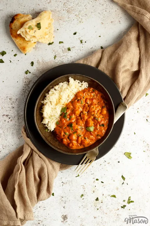 A bowl of chana masala curry and rice with a fork on a light brown napkin with torn naan bread at the side