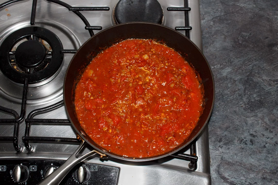 Chana masala curry base in a large saucepan with tinned tomatoes cooking on the stove