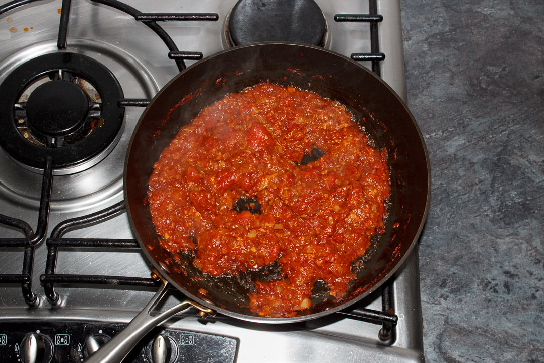 A reduced Chana masala curry base in a large saucepan cooking on the stove