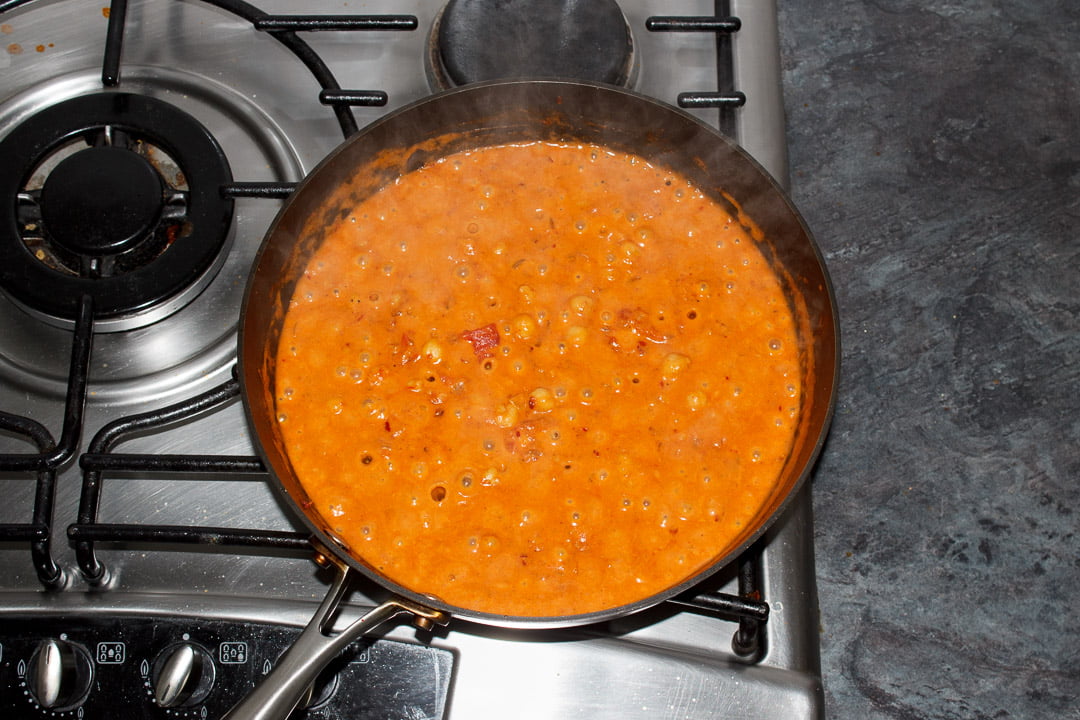 Chana masala curry base with coconut milk and chickpeas cooking in a large saucepan on a stove