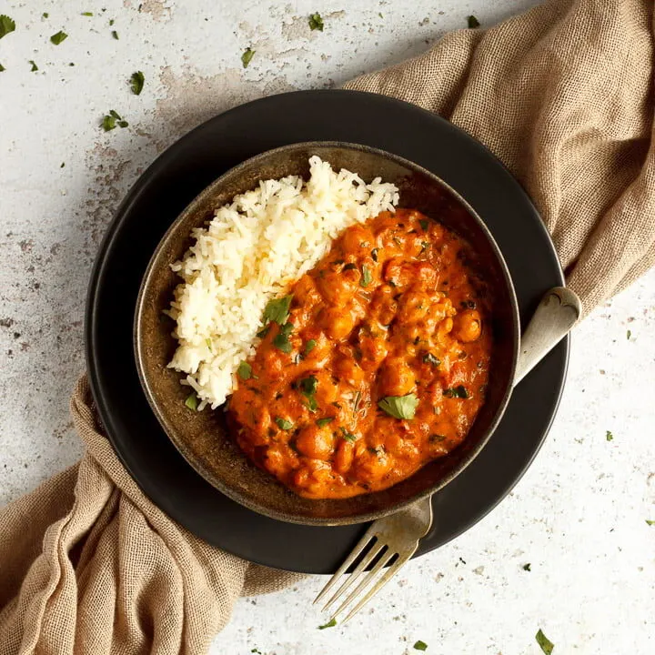 A bowl of chana masala curry and rice with a fork on a light brown napkin