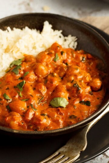 A bowl of chana masala curry and rice with a fork on a light brown napkin