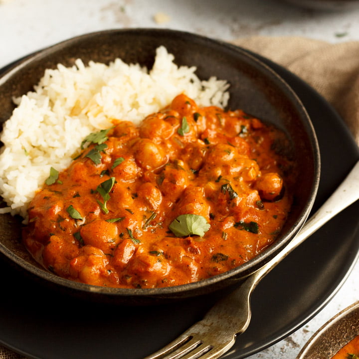 A bowl of chana masala curry and rice with a fork on a light brown napkin