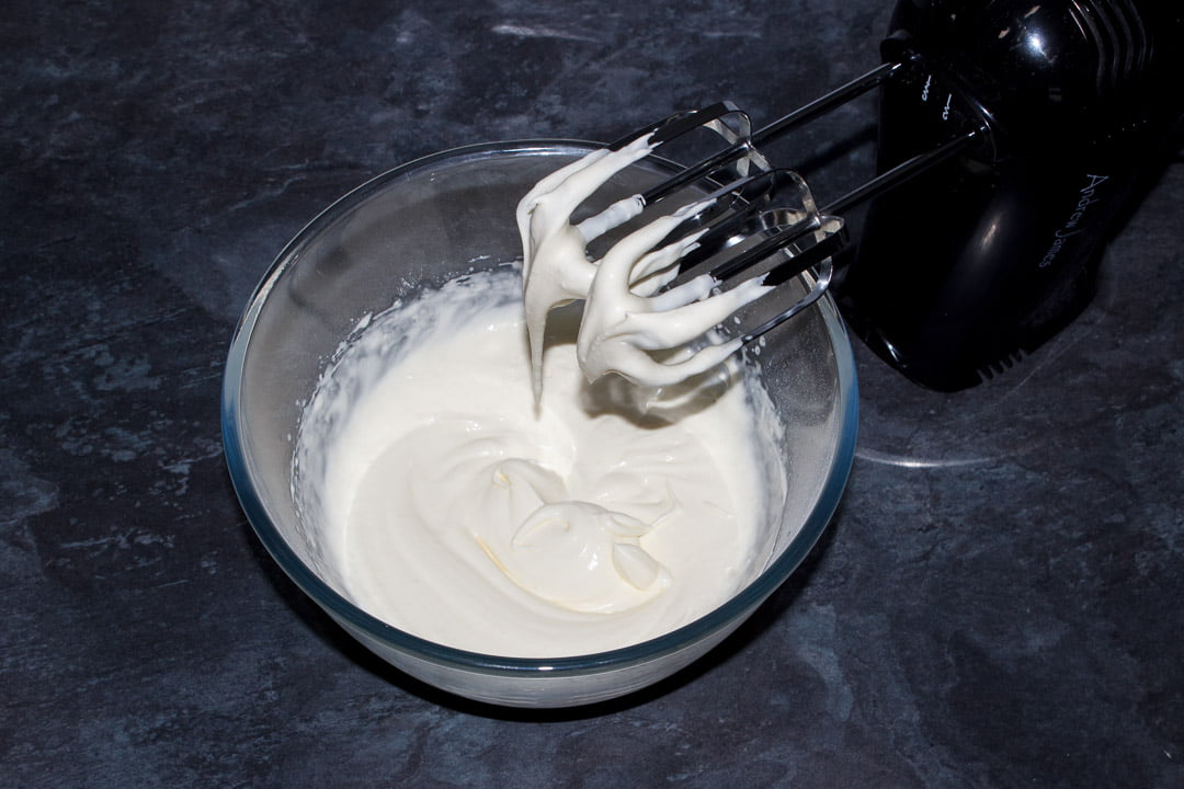 Cream and icing sugar whipped to soft peaks in a glass bowl with an electric hand whisk