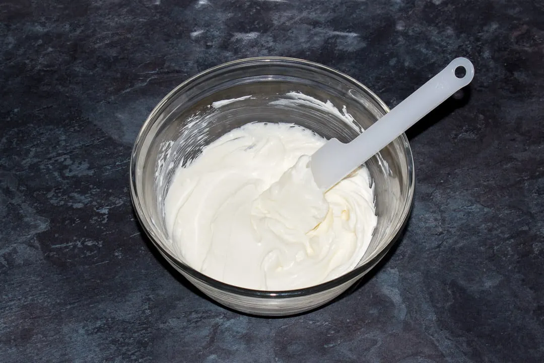 Softened cream cheese and sugar in a glass bowl with a spatula