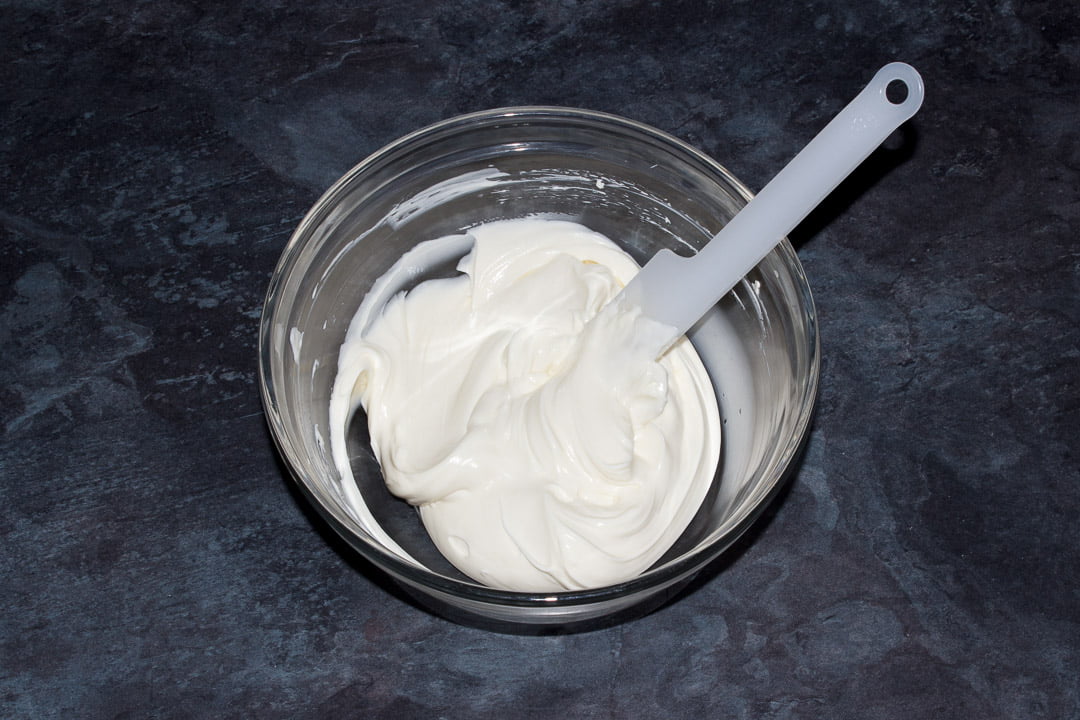 Cream cheese, sugar, soured cream and vanilla extract beaten together in a glass bowl with a spatula