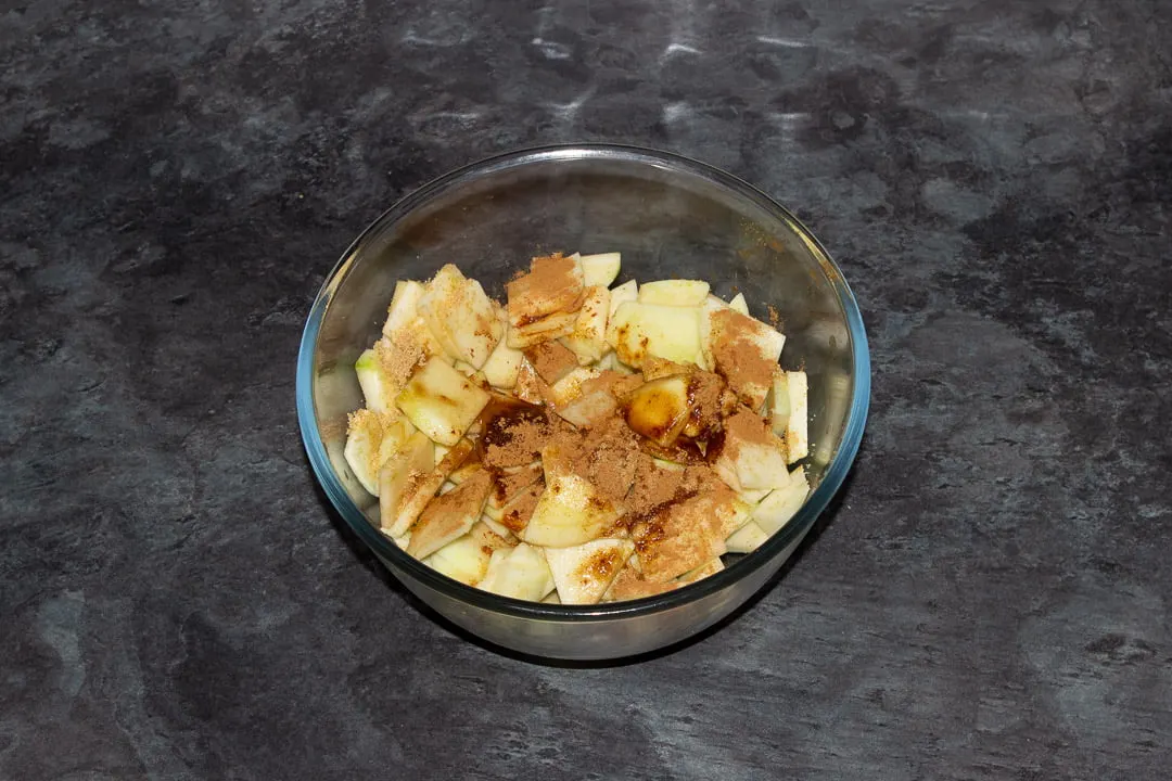Sliced apples in a glass bowl with sugar, vanilla, cinnamon and water