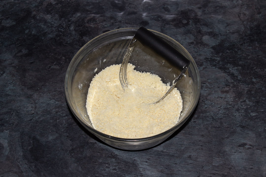 Crumble mixture in a glass bowl with a pastry blender