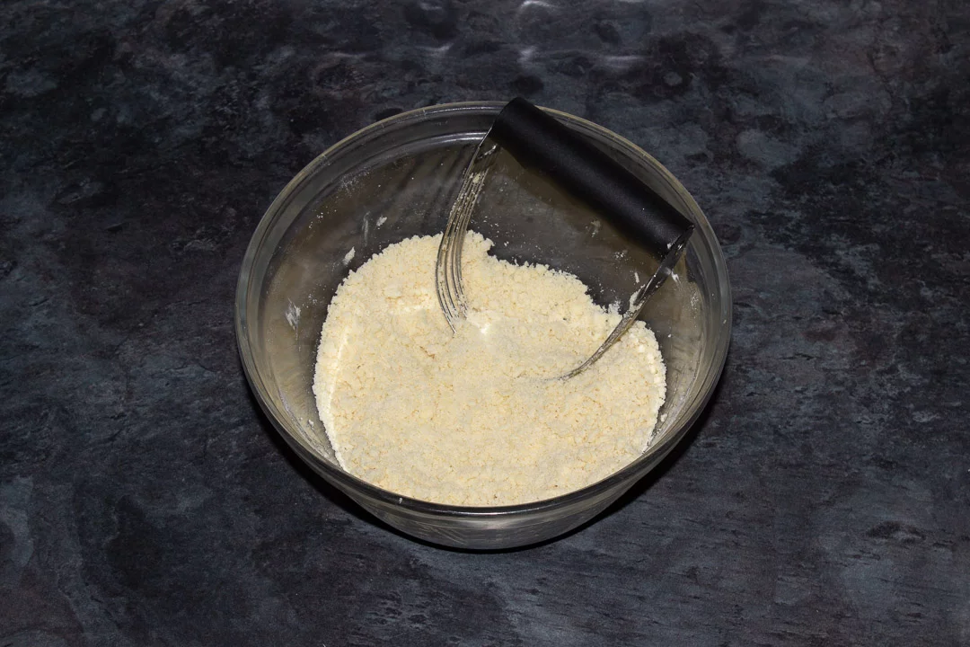 Crumble mixture in a glass bowl with a pastry blender