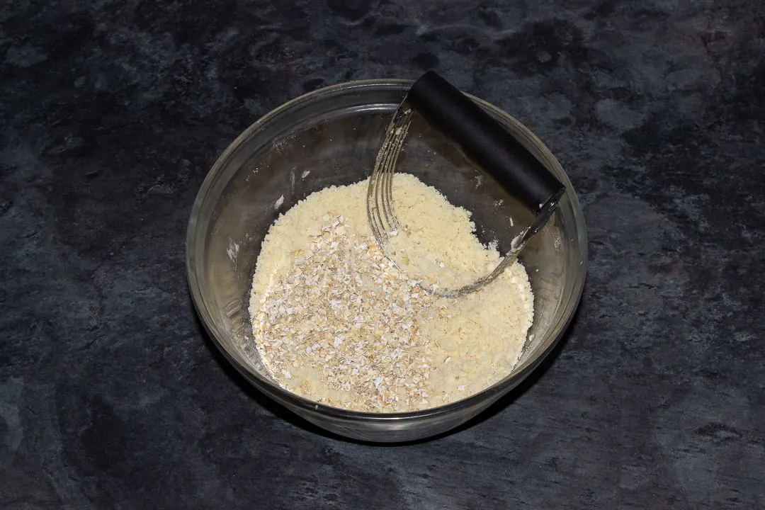 Crumble mixture with oats in a glass bowl with a pastry blender