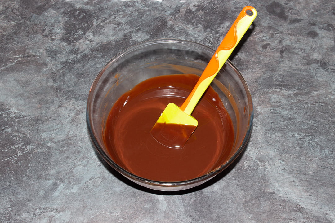 Melted dark chocolate and butter in a glass bowl with a rubber spatula