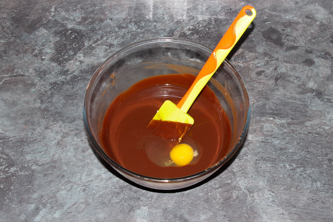 Melted dark chocolate, butter and eggs in a glass bowl with a rubber spatula