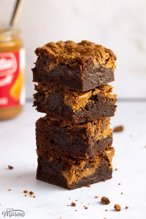 Biscoff brownies in a stack of 4 bars on a white work surface with a jar of Biscoff spread in the background