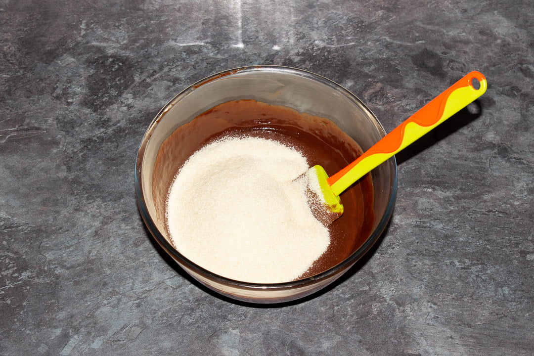 Melted dark chocolate, butter, eggs and sugar in a glass bowl with a rubber spatula