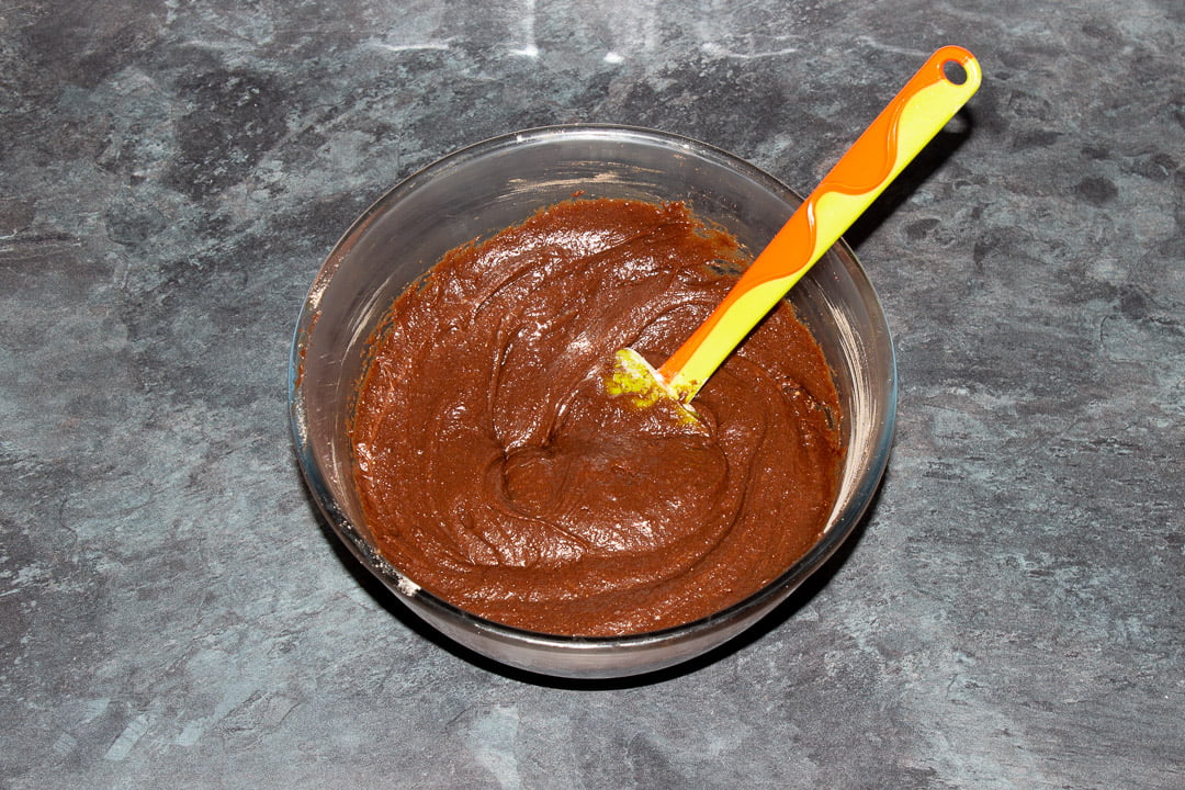 Brownie batter in a glass bowl with a rubber spatula