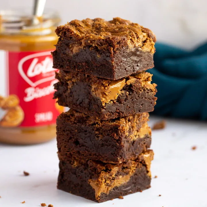 Biscoff brownies in a stack of 4 bars on a white work surface with a jar of Biscoff spread and a blue linen napkin in the background