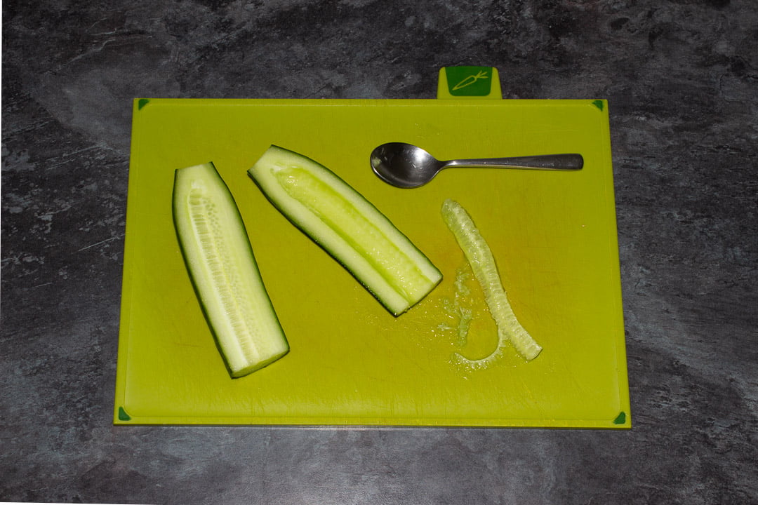 Halved cucumber on a green chopping board having the seeds scraped out