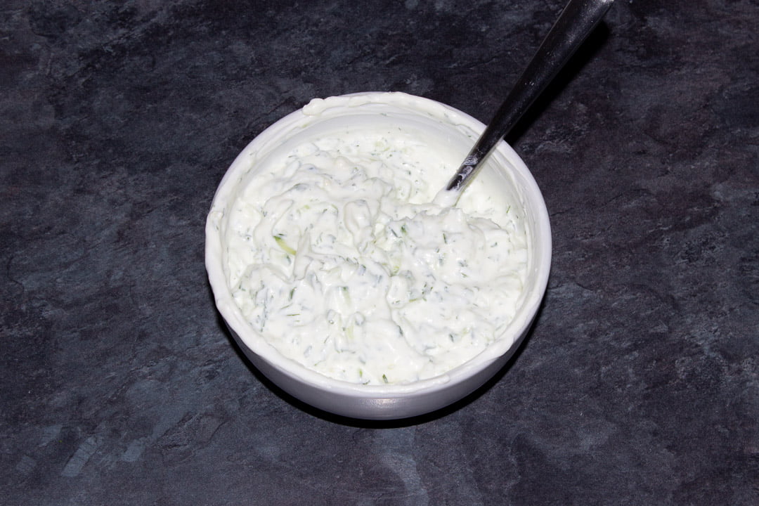 Finished tzatziki dip in a white bowl with a metal spoon