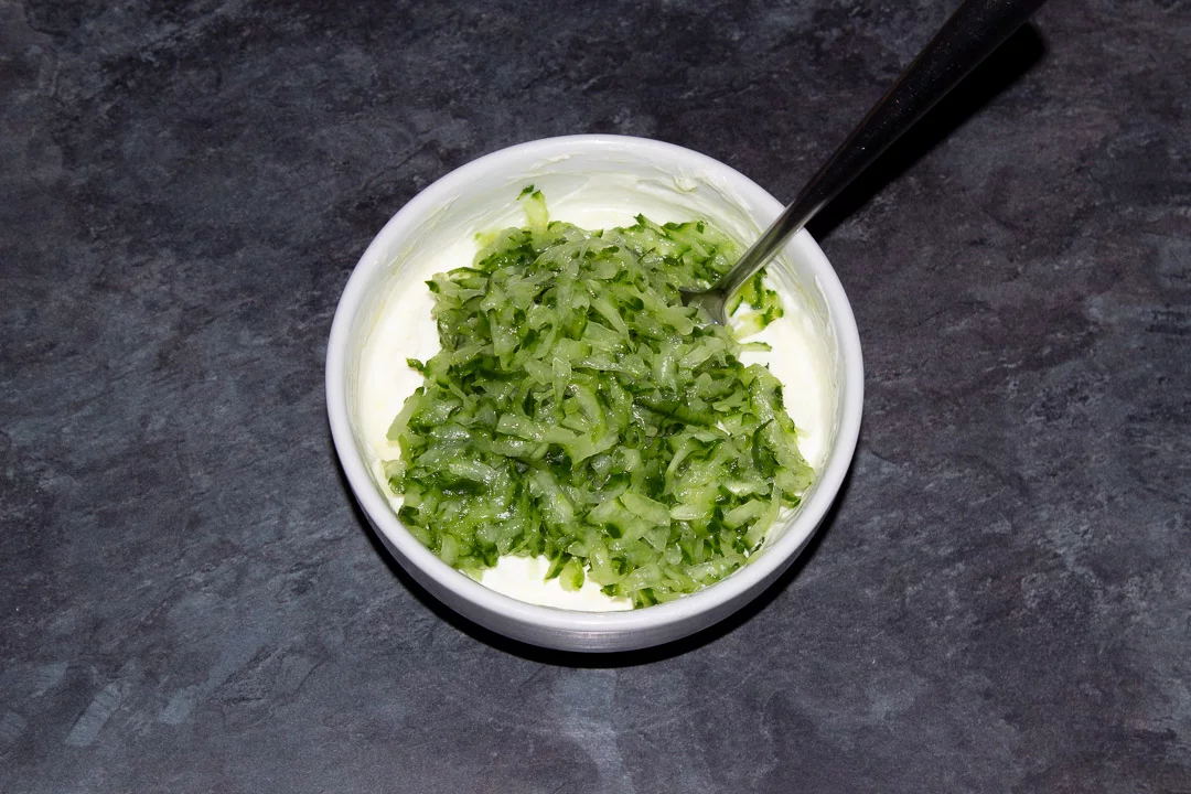 Drained, grated cucumber in a white bowl along with the remaining tzatziki ingredients (minus the dill).