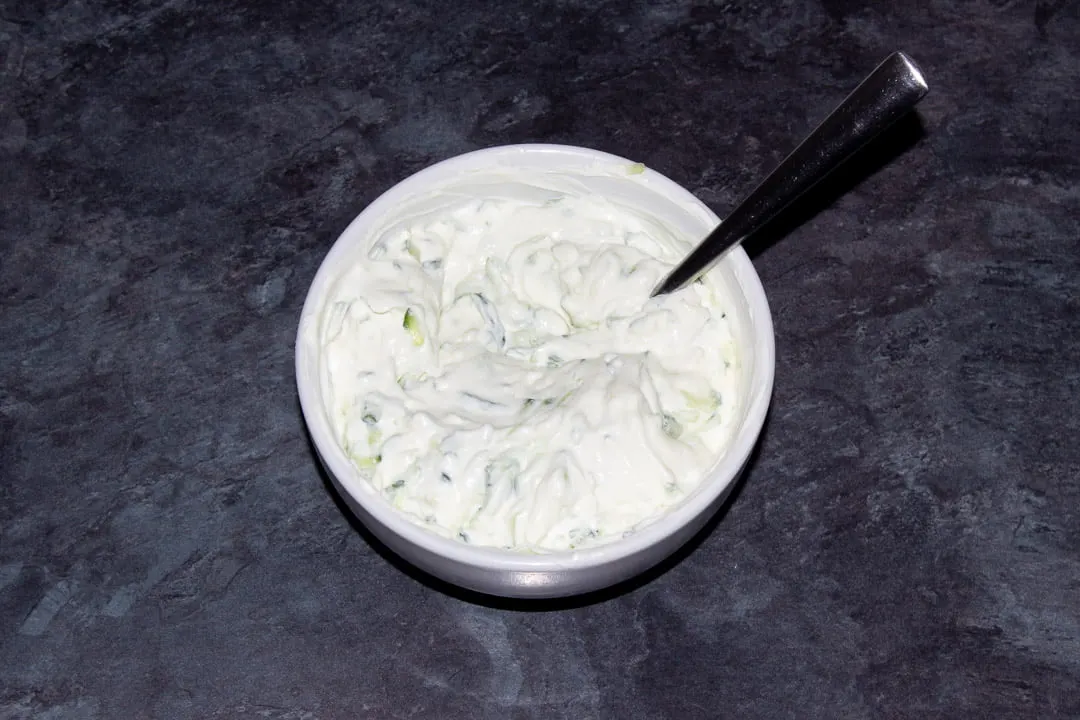 All the tzatziki ingredients (minus the dill) mixed together in a small white bowl
