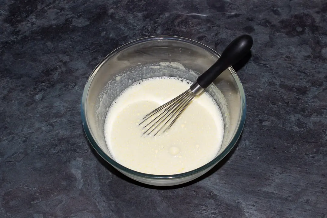 Vanilla custard base in a glass bowl with a whisk