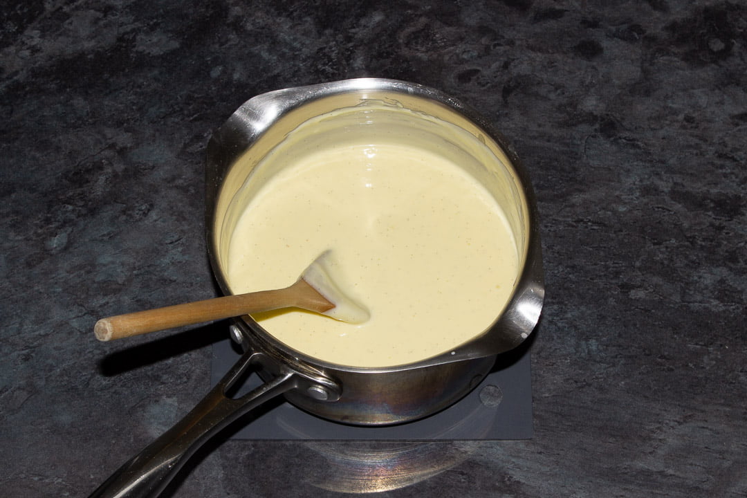 Homemade vanilla custard in a metal saucepan with a wooden spoon