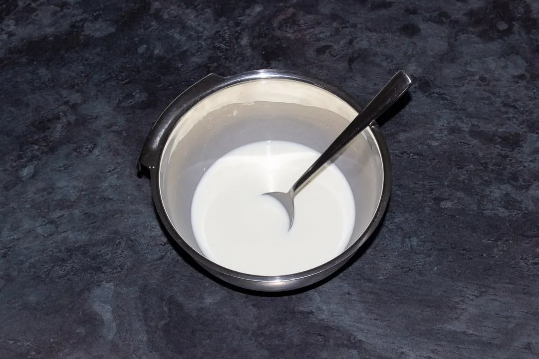 A milk and cornflour paste in a metal bowl with a metal spoon