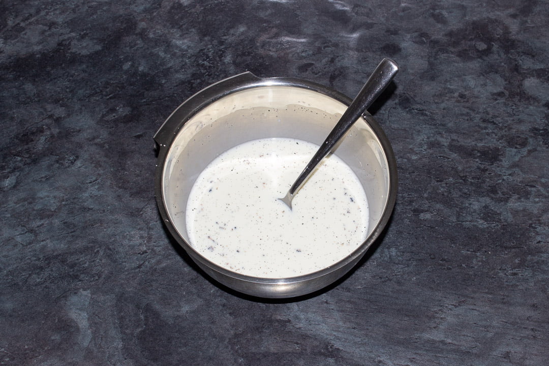 A vanilla infused milk and cornflour mixture in a metal bowl with a metal spoon