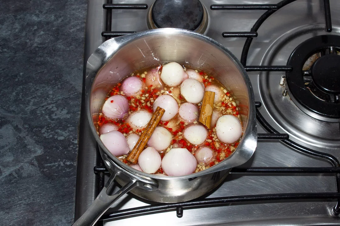 Peeled and trimmed baby shallots in a large saucepan on the stove with white wine vinegar, sugar, chilli, chinese 5 spice, ginger and cinnamon.