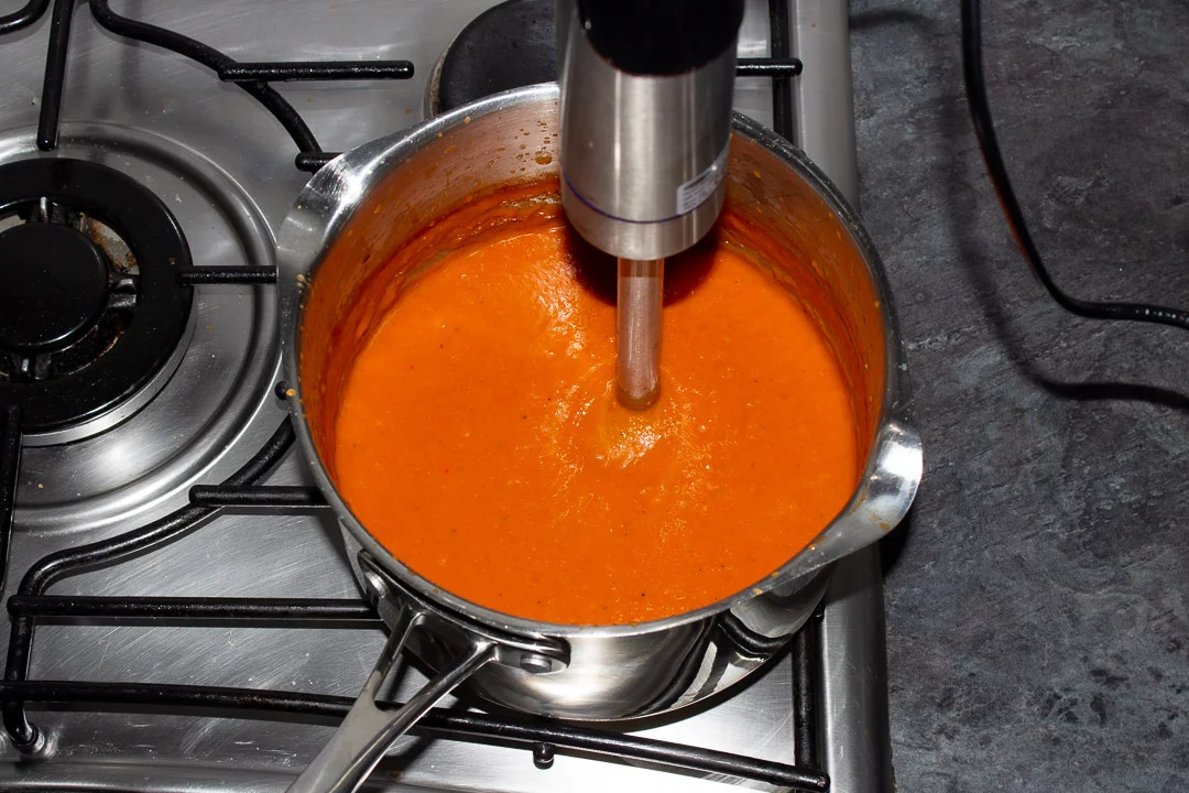 Tomato soup in a saucepan being blitzed with a stick blender