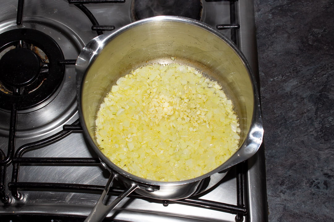 Onions and garlic frying in butter in a saucepan on a hob