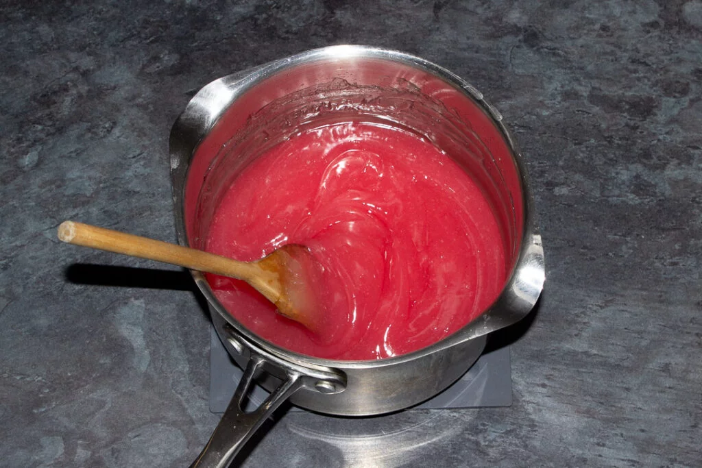 Turkish delight with added rosewater and red food colouring mixed together in a saucepan on a kitchen worktop with a wooden spoon inside