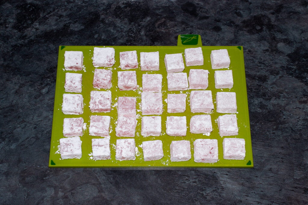 Turkish delight cubes coated in both cornflour and icing sugar set on a green chopping board