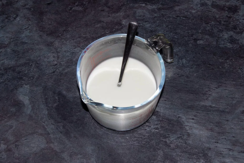 Cornflour dissolved in water in a glass jug with a metal teaspoon