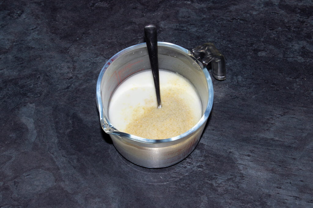 Cornflour dissolved in water with gelatine sprinkled on top in a glass jug with a metal teaspoon