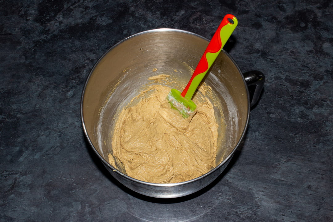 Biscoff blondies batter in the bowl of an electric stand mixer with a green and orange silicone spatula