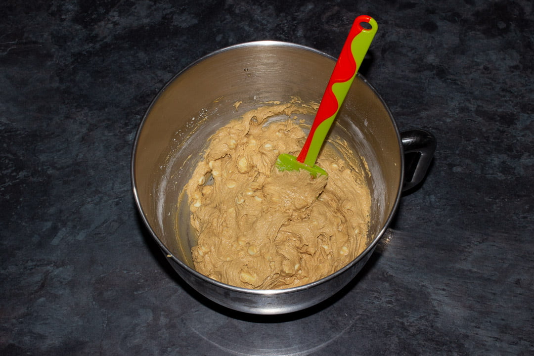 Biscoff blondies with added white chocolate chips batter in the bowl of an electric stand mixer with a green and orange silicone spatula
