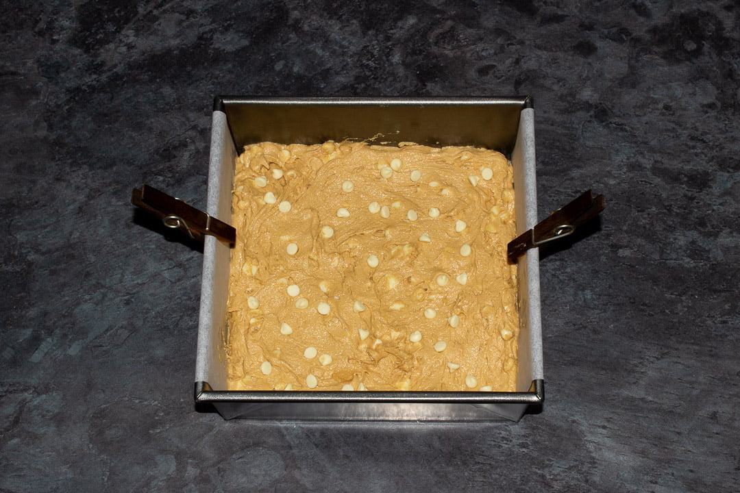 Biscoff blondie batter spread out in a lined square baking tin topped with white chocolate chips