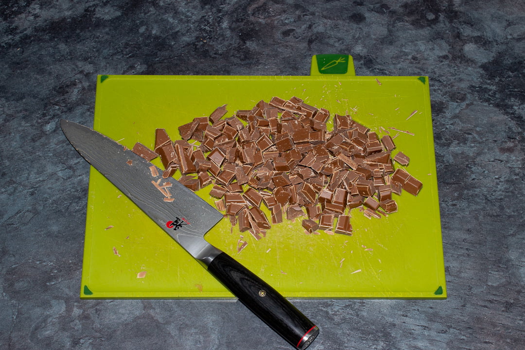 Chocolate chopped into chunks on a green chopping board with a sharp knife