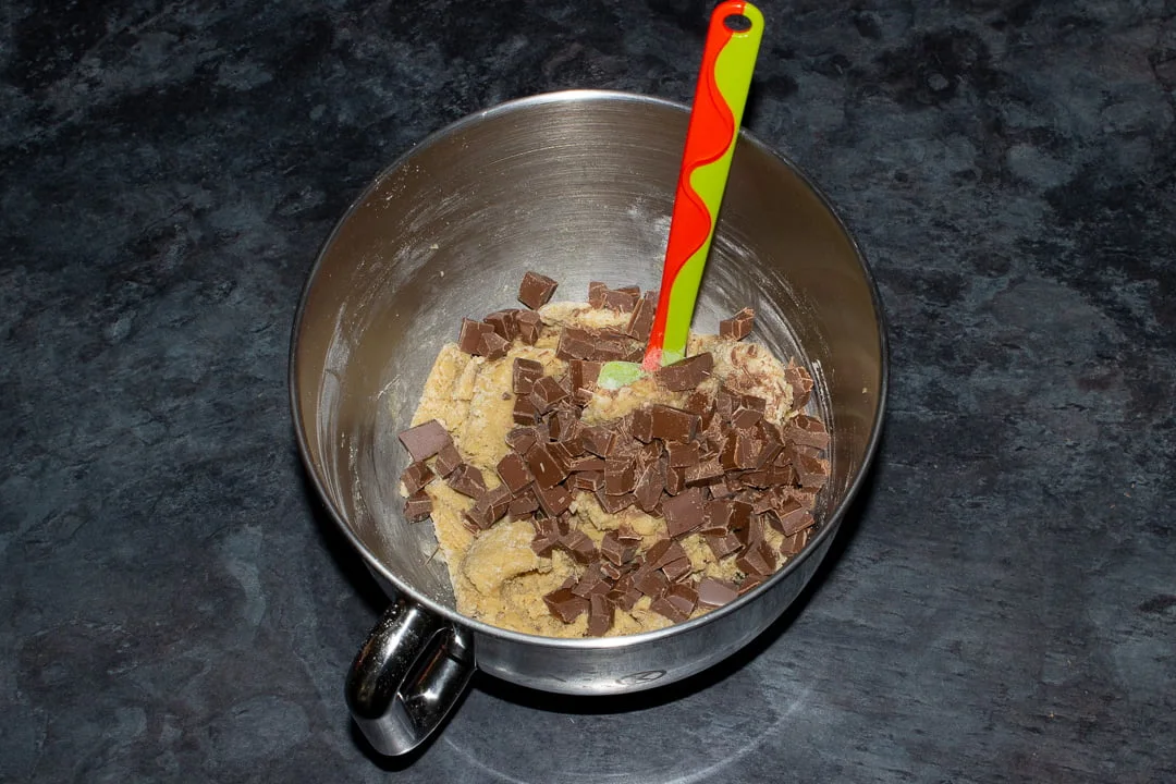 Cookie dough and chocolate chips in the bowl of en electric stand mixer with a green rubber spatula