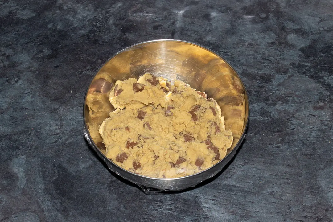 Chocolate chip cookie dough in a metal bowl covered with cling film