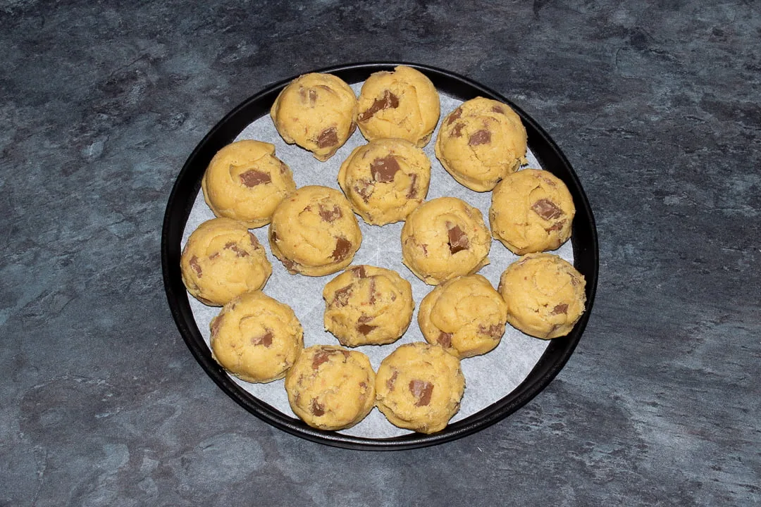Balls of chocolate chip cookie dough on a black plate lined with baking paper