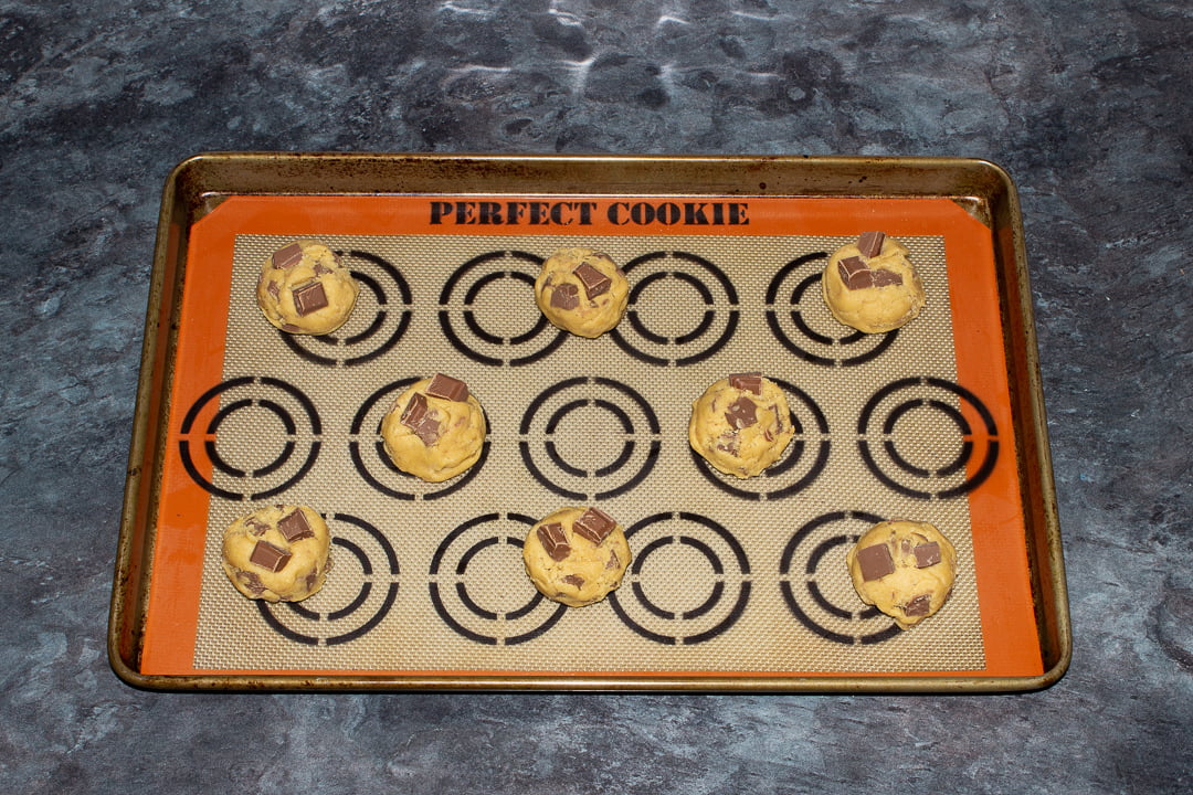 Chocolate chip cookie dough balls evenly spaced out on a lined baking tray