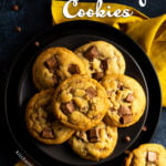 6 Chewy chocolate chip cookies on 2 stacked black plates set over a yellow linen napkin. With a deep blue marbled backdrop with more cookies and chocolate chips scattered around.