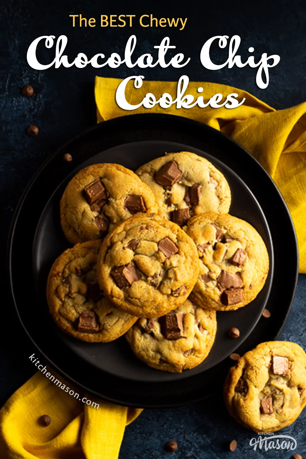 6 Chewy chocolate chip cookies on 2 stacked black plates set over a yellow linen napkin. With a deep blue marbled backdrop with more cookies and chocolate chips scattered around.