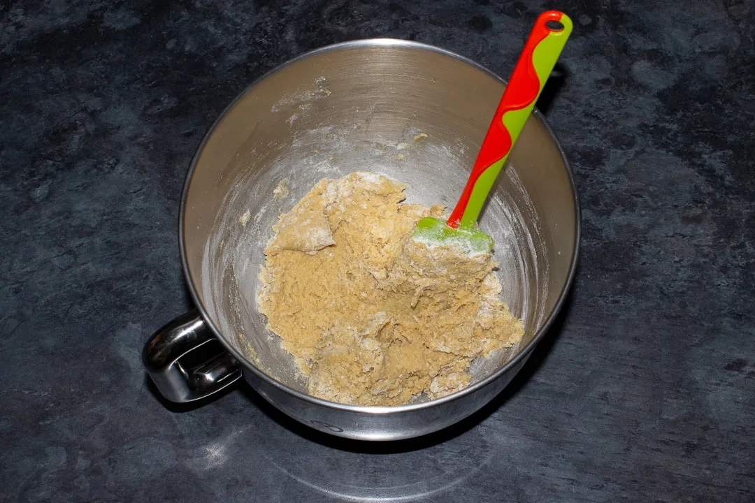 Cookie dough with half the flour mixture folded into it in the bowl of an electric stand mixer with a green rubber spatula